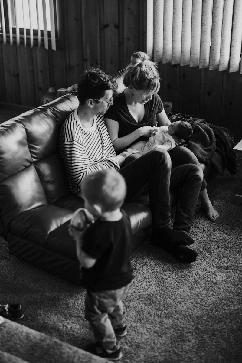 grayscale man and woman sitting on couch carrying baby